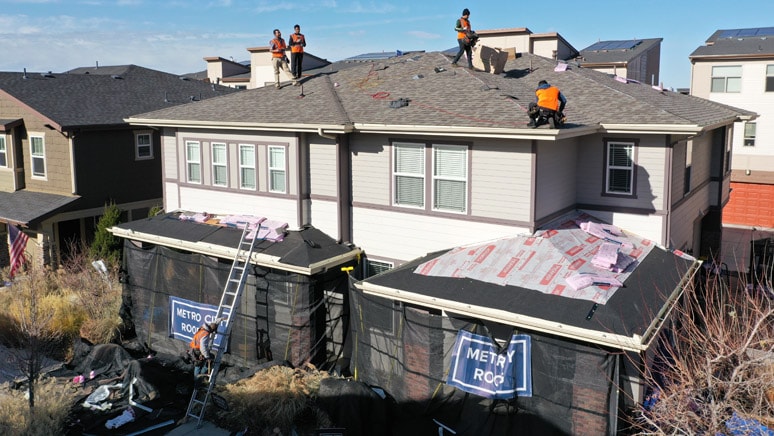 Metro City Roofing crew replacing the roof of a duplex in Denver, Colorado with five crew members working in orange vests with landscape protection kit in the front of the duplex