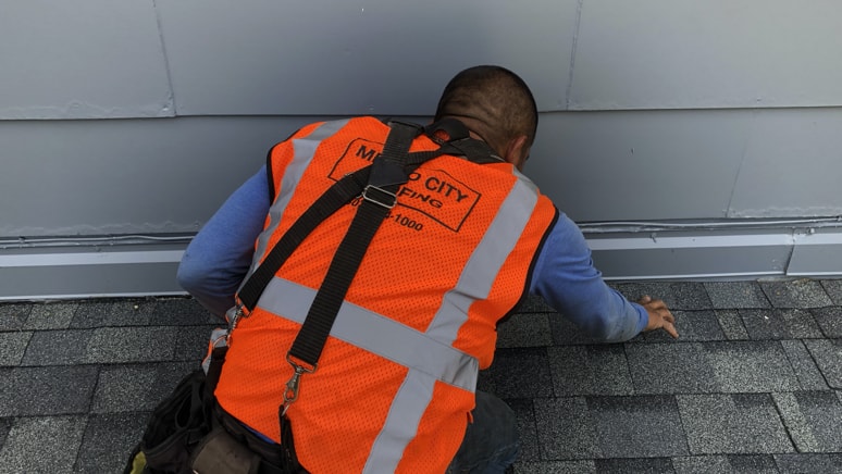 Metro City Roofing crew member in an orange vest adding silicone caulk to seal exposed nailheads on a roof in Littleton, Colorado