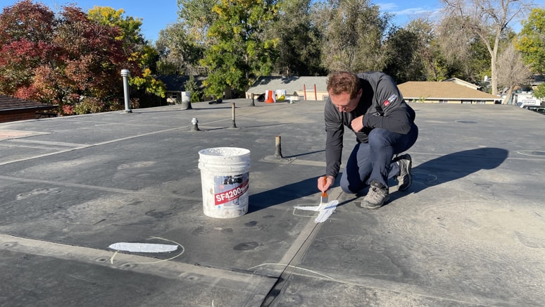Metro City Roofing installer repairing an EPDM flat roof with Gaco silicone sealant.